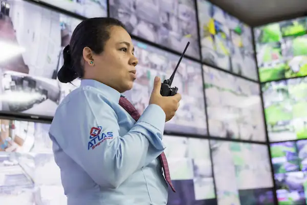 Operadora de central de monitoreo Atlas Seguridad comunicándose por radio frente a pantallas de vigilancia en Bogotá