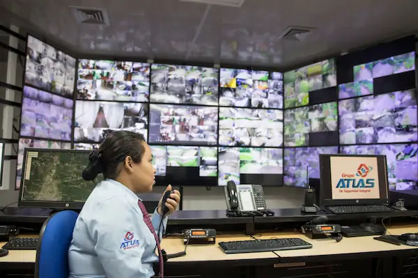Operadora sentada en central de monitoreo Grupo Atlas con múltiples pantallas de vigilancia y equipos de comunicación